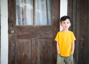 little boy in yellow shirt in front of brown door