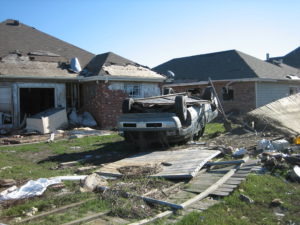 overturned car in front of house destroyed by hurricane