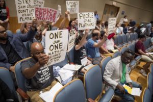 protesters with signs seated in the back of a conference room