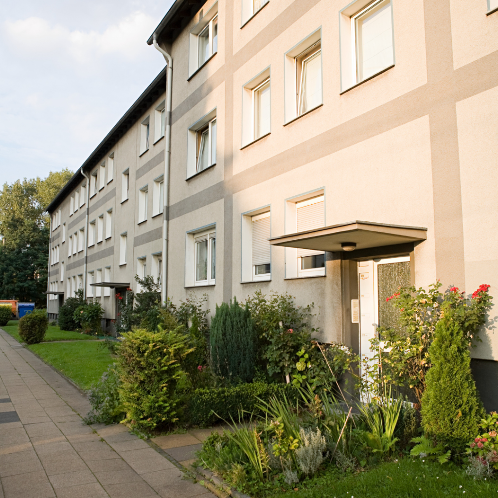 the entranceway to a tan colored apartment building with bushes by the doorway