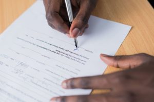 hands of an african american man signing a document on a wooden table