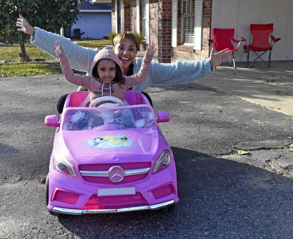 Smiling young girl in pink toy car with arms up. Her mother is behind her with her arms up in joy as well. Arielle Butler and her daughter, who were denied an apartment in Zachary, LA due to an eviction record
related to unemployment during COVID-19. Source: Hilary Scheinuk, The Advocate.