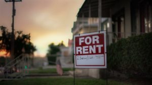 for rent sign with houses and front lawns blurred in the background